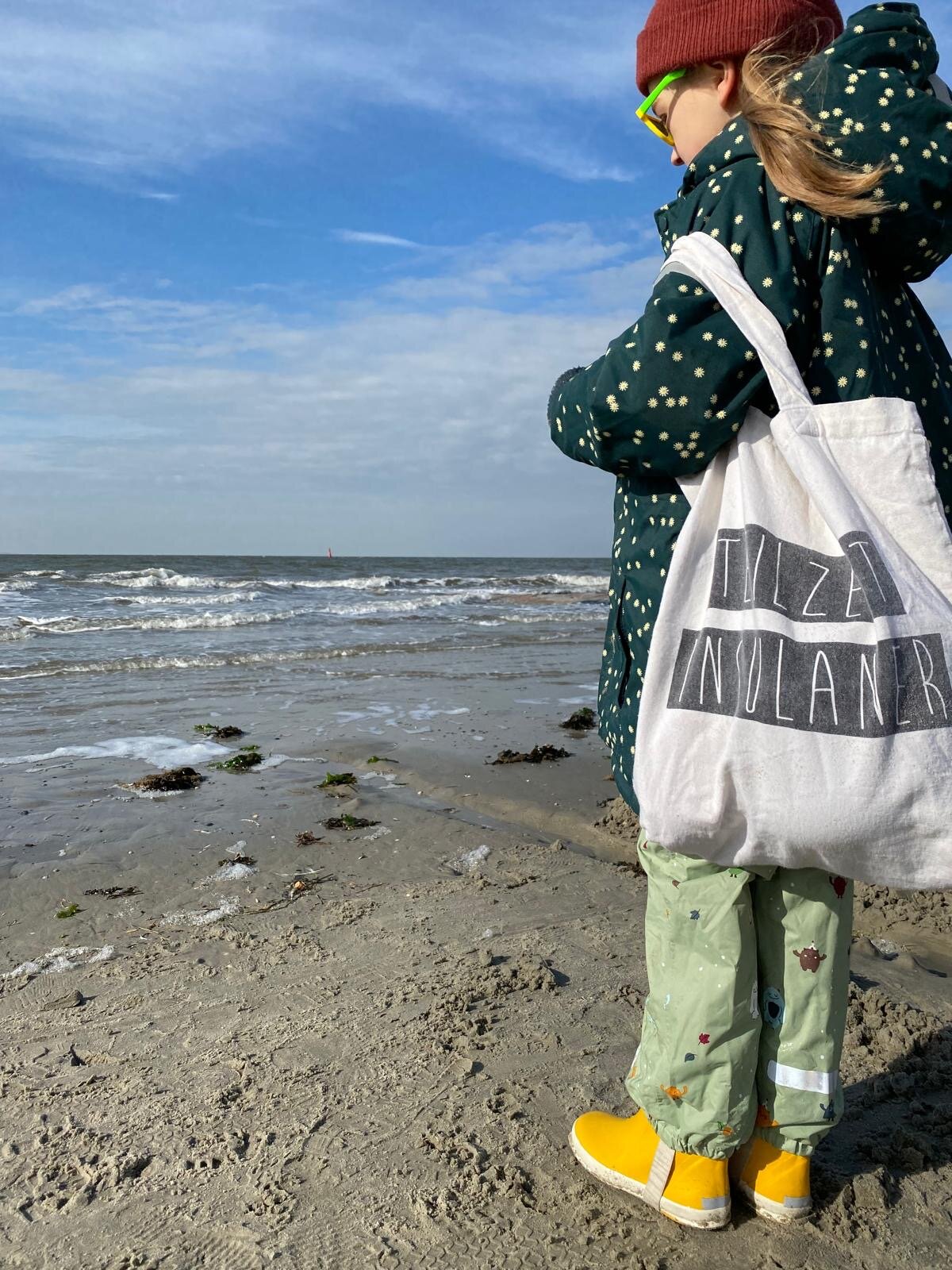 Kind mit Umhängetasche blickt aufs Meer